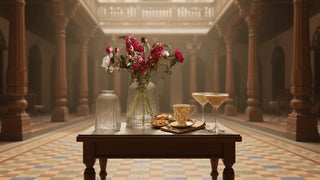 Decorative table setting with flowers, glasses, and snacks in a grand hall.